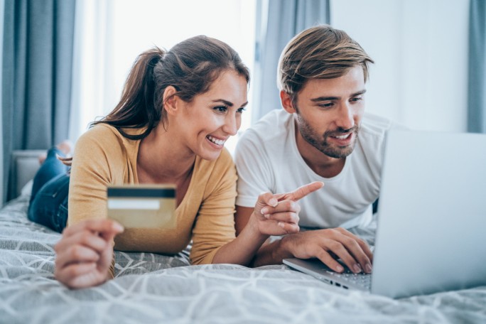 Nasmejani par koristi laptop za sigurnu online kupovinu uz 3D Secure zaštitu prilikom plaćanja karticom iz kreveta