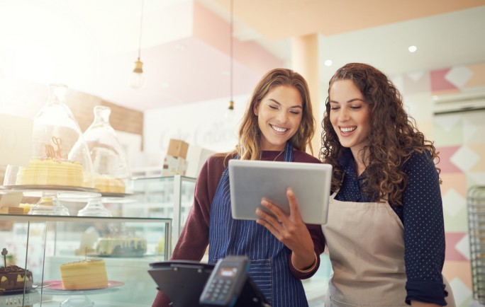 Dve devojke na poslu gledaju  na tabletu kako se uvode POS terminali