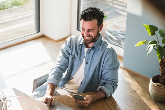 Nasmejani muškarac koristi laptop i telefon za online investiranje u Raiffeisen investicione fondove od kuće