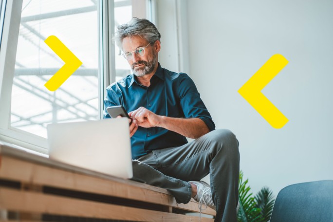 Čovek analizira opcije za dugoročnu štednju i investiranje na laptopu i mobilnom telefonu iz kancelarije