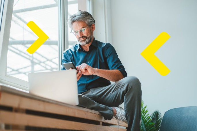 Čovek analizira opcije za dugoročnu štednju i investiranje na laptopu i mobilnom telefonu iz kancelarije