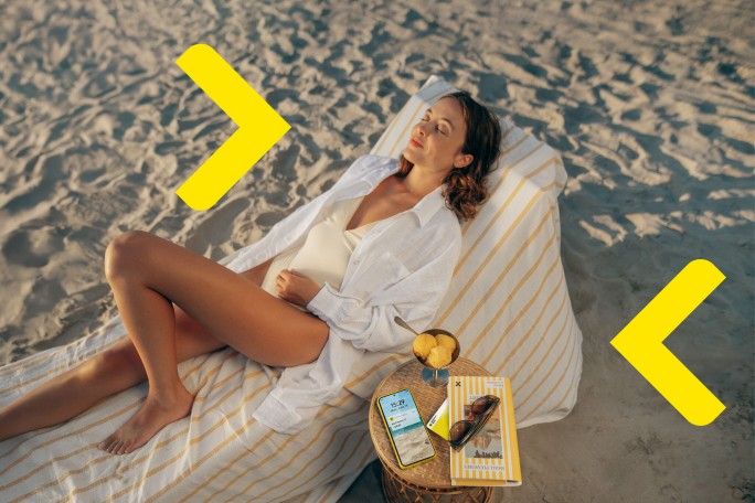Žena odmara na plaži i koristi kreditnu karticu Raiffeisen banke za brza i sigurna plaćanja
