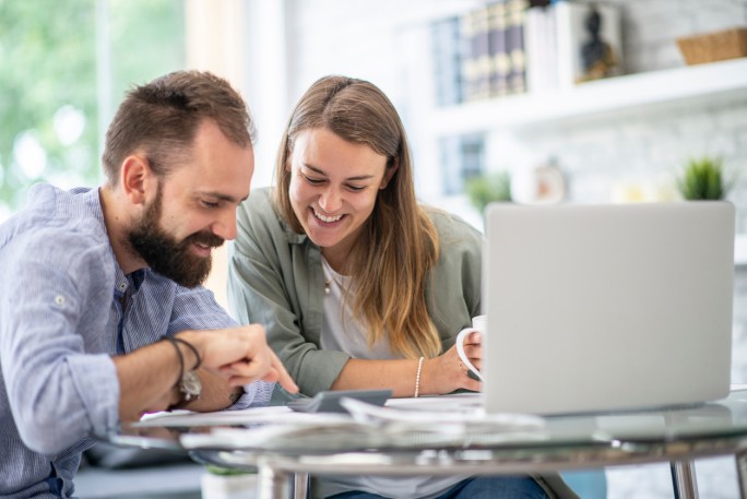 Nasmejani par koristi laptop i digitron za proveru kursne liste u online menjačnici.