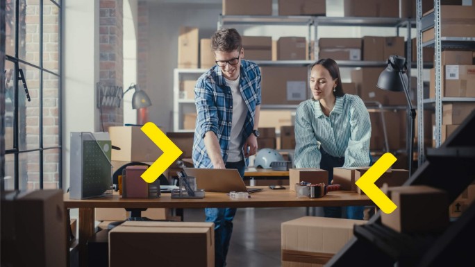 Young entrepreneurs in a warehouse using a laptop to plan new equipment procurement with a Raiffeisen Bank investment loan