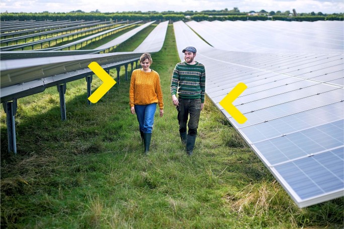 Mladi par šeta kroz polje sa solarnim panelima planirajući održivu investiciju uz povoljan kredit za solarne panele