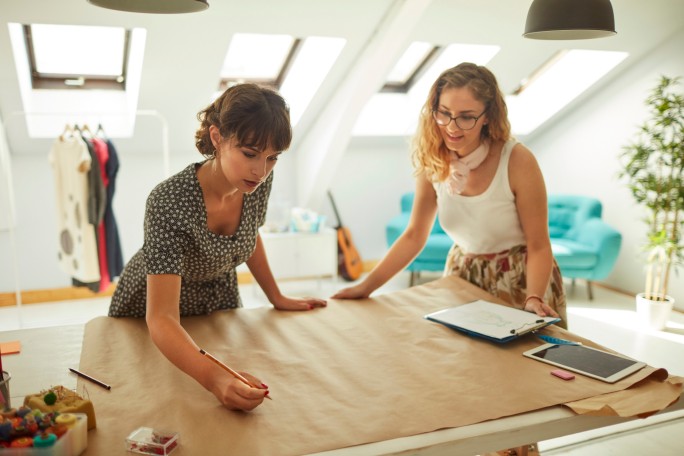 Two young female fashion designers working together in their workshop.