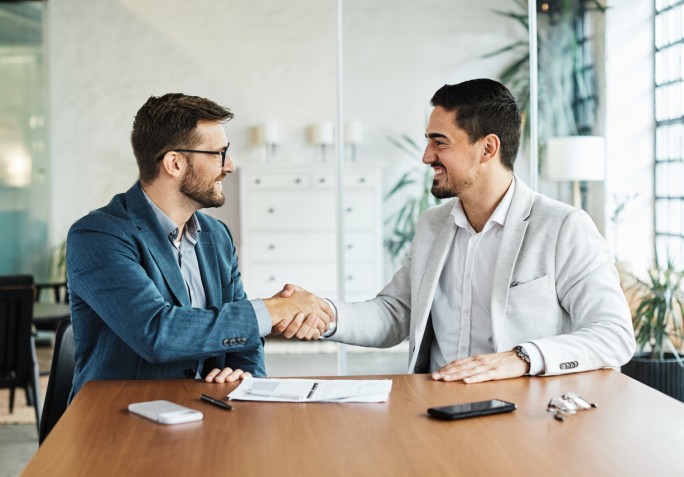 Two happy young businessman shaking hands after signing a contract in the office